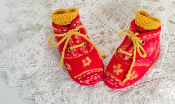 Red baby booties felted with yellow laces on the lace doily. — Stock Photo, Image