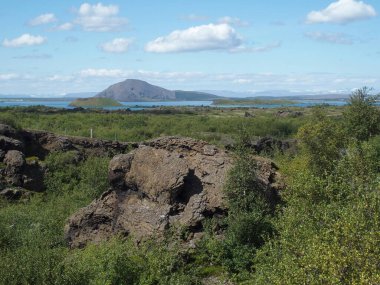 İzlanda, Dimmuborgir 'de serinletilmiş bir lav gölünün kalıntıları, arka planda Myvatn Gölü ve büyük, tuhaf şekiller oluşturur.
