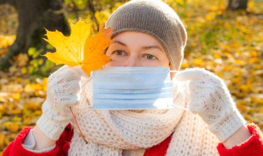 Komik kıdemli kadın sonbahar parkının arka planında koruyucu maske tutuyor..