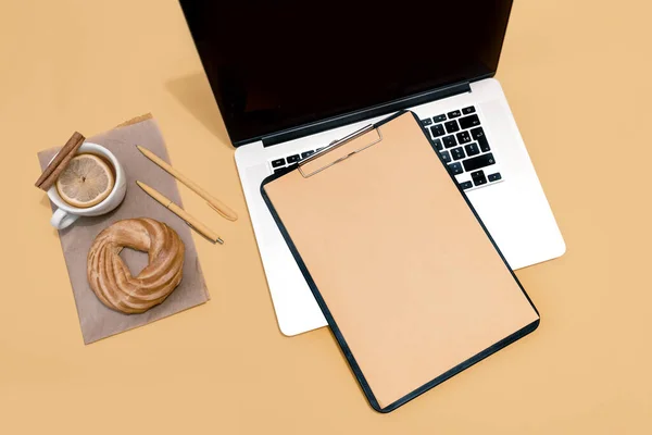 Laptop, cake, cup of tea and resume sheet on the pastel orange table, top view.