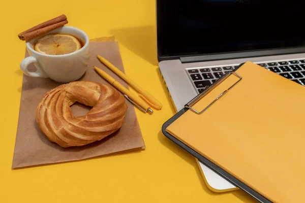 Laptop, cake, cup of tea and resume sheet on the Fortuna Gold Yellow Colour Background, top view.