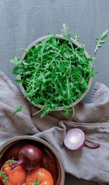 Taze yeşil roka, gri arka planda soğan ve domates tabağı..