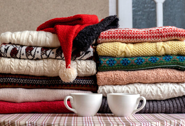 A Lot of Sweaters and Pullovers Different Colours folded in two Piles on the Table with two cups of coffee.