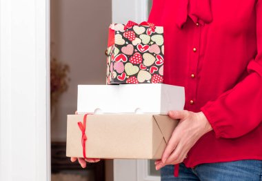 Sevgililer Günü 'nün kırmızı kalpleri ve beyaz kapının yanında hediye kutuları olan alışveriş torbası tutan kadının elleri..