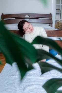 Beyaz kazak giymiş orta yaşlı bir kadın yatak odasında yerde oturuyor.