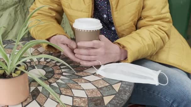 Weibliche Hände Mit Kaffeebecher Und Medizinischer Gesichtsmaske Frau Sitzt Draußen — Stockvideo