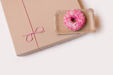 Kağıt teslimat kutusunda pembe kek, beyaz arka planda kırmızı fiyonk, üst görünümde..
