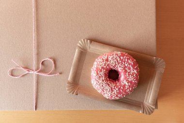 Kağıt teslimat kutusunda pembe pasta, ahşap arka planda kırmızı fiyonk, üst manzara..
