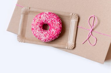 Kağıt teslimat kutusunda pembe kek, beyaz arka planda kırmızı fiyonk, üst görünümde..