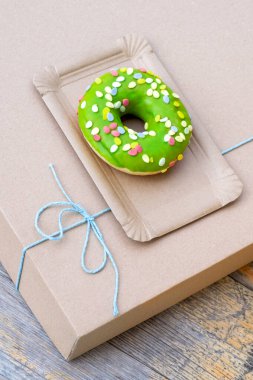 Kağıt teslimat kutusunda yeşil pasta, ahşap arka planda mavi fiyonk, üst manzara..