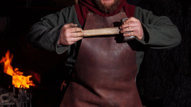 Viking demircide silah ve kılıç dövüyor. Demircide savaşçı kıyafeti giymiş bir adam var.