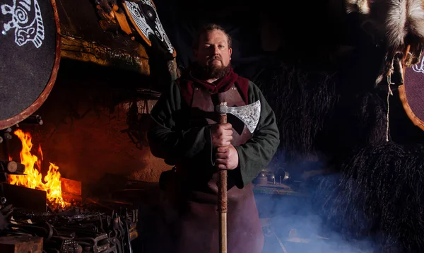 Viking forges weapons and swords in the smithy. A man in a warrior\'s clothes is in the smithy on the background of fire.