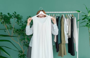 Orta yaşlı kadın alışveriş yapıyor ve rafın yanındaki elbiseye bakıyor..