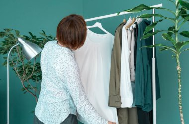 Orta yaşlı kadın alışveriş yapıyor ve rafın yanındaki elbiseye bakıyor..