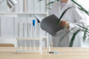 Doktor test tüpleri, ampul ve şırınga ile masanın yanında duruyor. Küresel aşı kavramı..