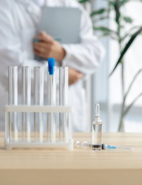 Doktor test tüpleri, ampul ve şırınga ile masanın yanında duruyor. Küresel aşı kavramı..
