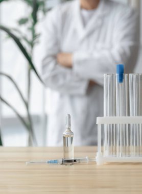 Doktor test tüpleri, ampul ve şırınga ile masanın yanında duruyor. Küresel aşı kavramı..