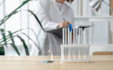 Doktor test tüpleri, ampul ve şırınga ile masanın yanında duruyor. Küresel aşı kavramı..