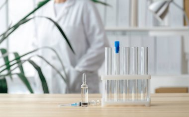 Doktor test tüpleri, ampul ve şırınga ile masanın yanında duruyor. Küresel aşı kavramı..