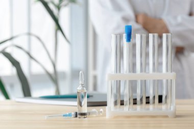 Doktor test tüpleri, ampul ve şırınga ile masanın yanında duruyor. Küresel aşı kavramı..