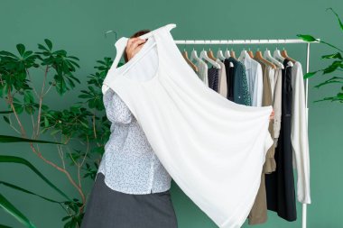 Orta yaşlı kadın alışveriş yapıyor ve rafın yanındaki elbiseye bakıyor..