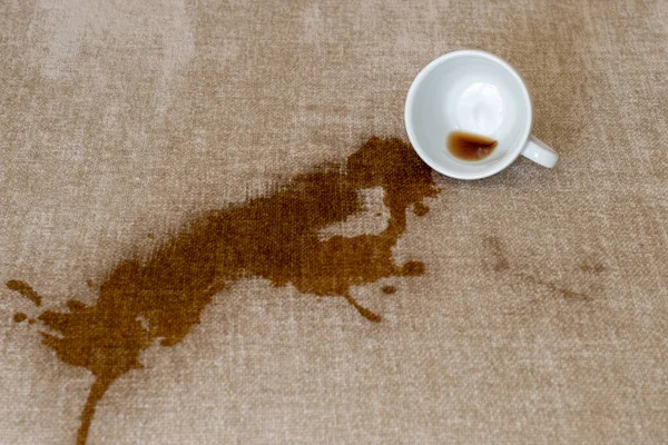 Spilled cup of coffee on the sofa with dirty stain.