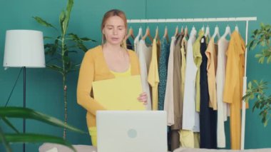 Orta yaşlı sarışın kadın dizüstü bilgisayarla iletişim kuruyor ve rafta giysilerini gösteriyor..