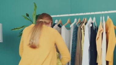 Orta yaşlı sarışın kadın alışveriş yapıyor ve rafın yanındaki yeni kıyafetlere bakıyor.