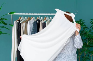 Orta yaşlı kadın alışveriş yapıyor ve rafın yanındaki elbiseye bakıyor..