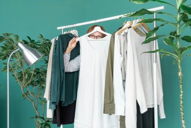 Orta yaşlı kadın alışveriş yapıyor ve rafın yanındaki elbiseye bakıyor..