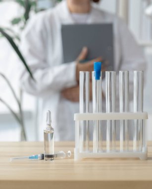 Doktor test tüpleri, ampul ve şırınga ile masanın yanında duruyor. Küresel aşı kavramı..