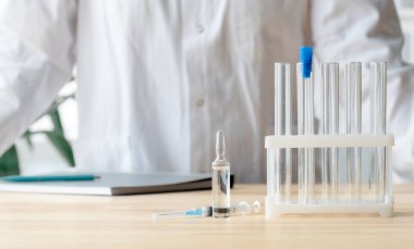 Doktor test tüpleri, ampul ve şırınga ile masanın yanında duruyor. Küresel aşı kavramı..