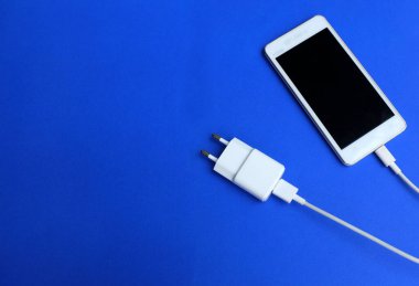 Üst görünüm, mavi arkaplanda bir USB kablosu ile akıllı telefonu şarj ediyor