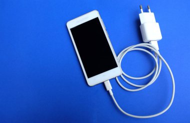 Üst görünüm, mavi arkaplanda bir USB kablosu ile akıllı telefonu şarj ediyor