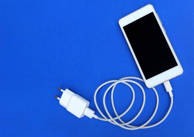 Üst görünüm, mavi arkaplanda bir USB kablosu ile akıllı telefonu şarj ediyor