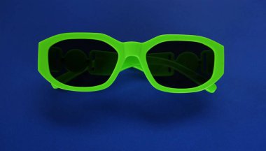 Modern yeşil güneş gözlükleri mavi bir arka planda izole edilir. Gezgin ve yaz aksesuarları.