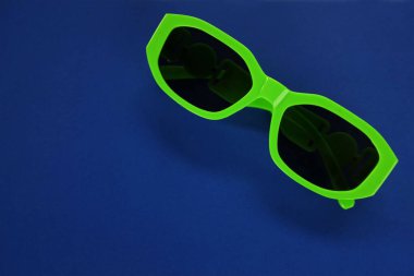 Modern yeşil güneş gözlükleri mavi bir arka planda izole edilir. Gezgin ve yaz aksesuarları.