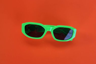 Çağdaş yeşil güneş gözlüklerini kapat turuncu bir arka planda izole et. Gezgin ve yaz aksesuarları.