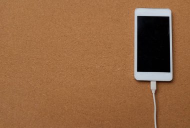 düz uzanmış akıllı telefon kahverengi arkaplandaki şarj cihazına bağlanır.