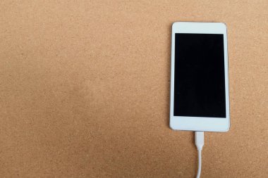 düz uzanmış akıllı telefon kahverengi arkaplandaki şarj cihazına bağlanır.
