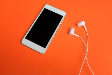 Turuncu arka planda akıllı telefon ve kulaklıkları kapat