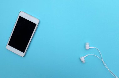 top view and copy space white Smartphone with Earphones on Blue Background .