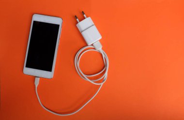 Close up and top view white Smartphone Connects with Charger on Orange Background