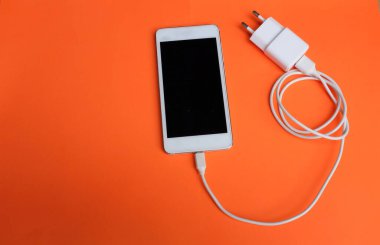 Close up and top view white Smartphone Connects with Charger on Orange Background