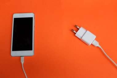 Close up and top view white Smartphone Connects with Charger on Orange Background