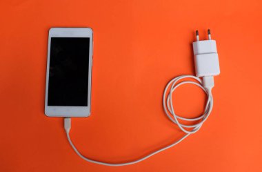Close up and top view white Smartphone Connects with Charger on Orange Background