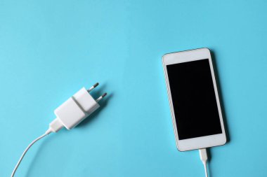 Close up and top view Smartphone Connects with Charger on blue Background 