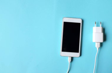 Close up and top view Smartphone Connects with Charger on blue Background 