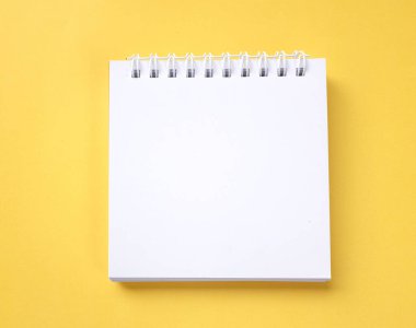 düz yatış ve üst görünüm boş beyaz spiral not defteri bir masa sarı arka plan üzerinde.