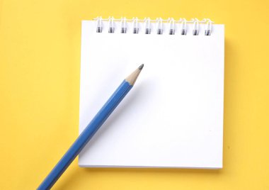 Masa sarı arka planda beyaz spiral bir not defterine düz bir kalem.